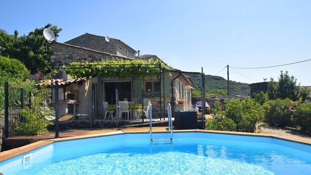 A swimming pool with a wooden deck, a stone building with a balcony, and a garden area with chairs and tables. - Relaxing Retreat in Saint-pons (Saint-Pons)