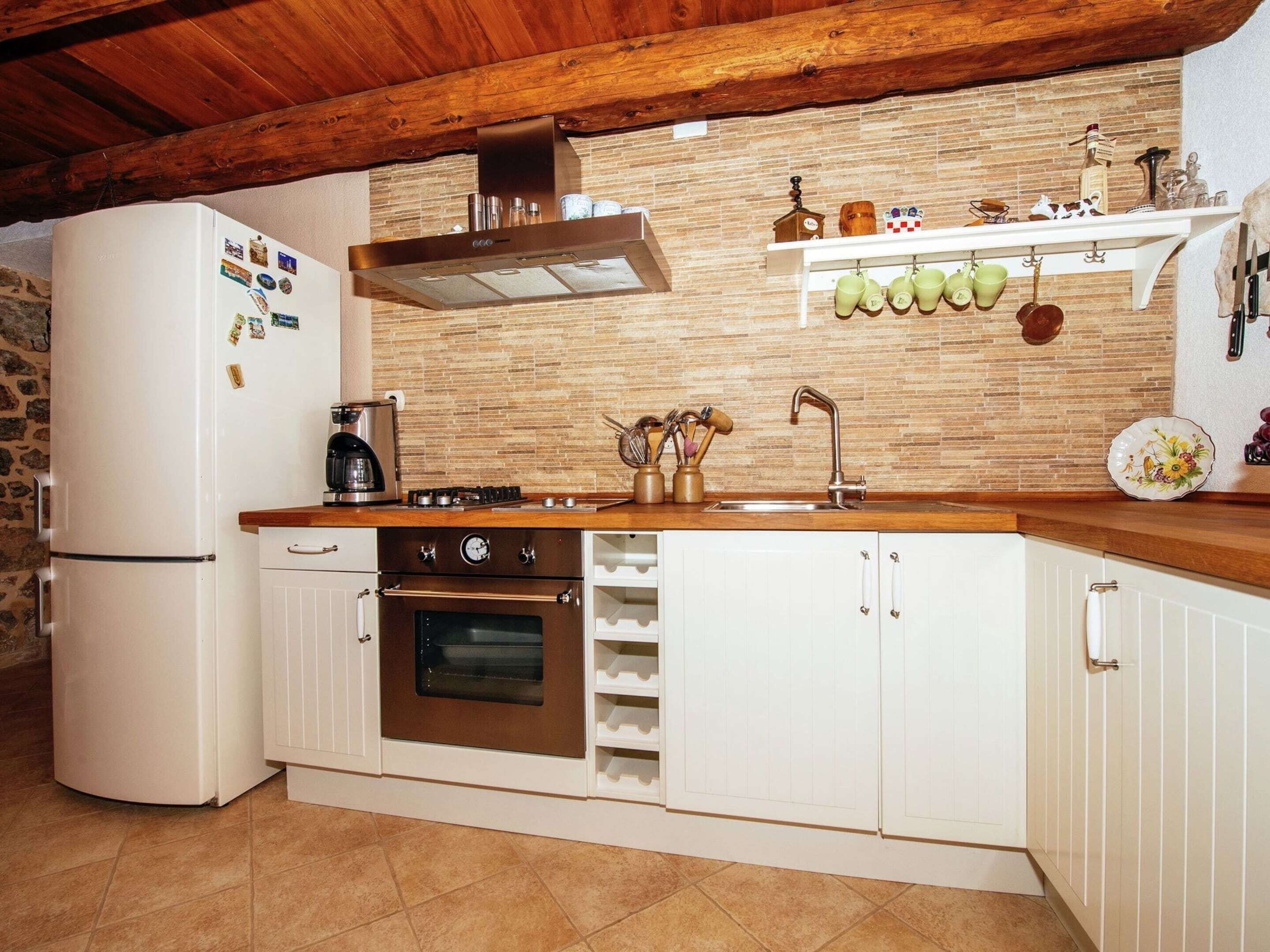 Cozinha com forno embutido, geladeira, bancada de madeira e painel de parede em tijolos.