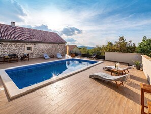 Relax by the serene pool surrounded by lush trees and a distant hill view.
