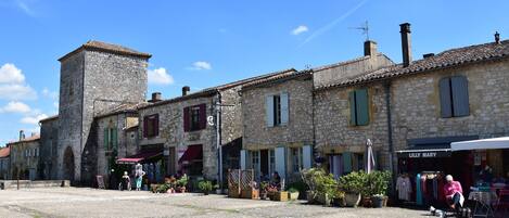 A stone building with a tower, a shop named 'Lilly Mary,' and outdoor seating with plants.