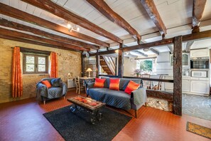 A rustic interior with exposed wooden beams, a sofa set, a coffee table, and a kitchen in the background. - Cosy Holiday Home With Garden (Villefranche-du-Perigord)
