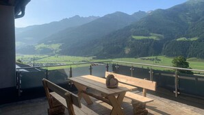 A wooden table and benches on a balcony with a mountain view. - Warm Apartment in Uttendorf Salzburg near Ski Area (Uttendorf)
