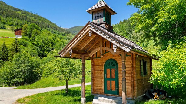 A small wooden chapel with a green door and a bell tower, surrounded by lush greenery and a clear sky. - Warm Apartment in Uttendorf Salzburg near Ski Area (Uttendorf)