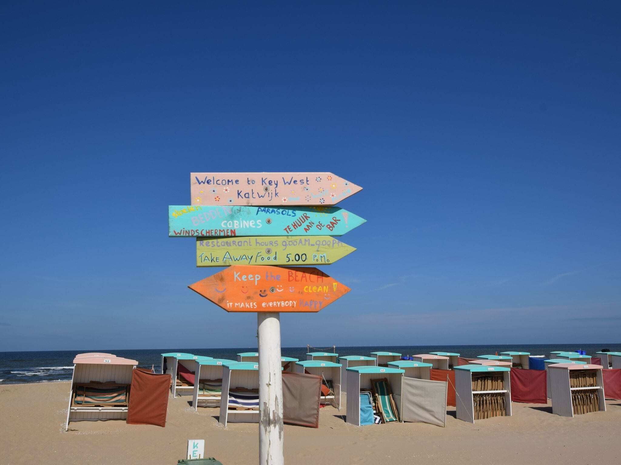 A beach with a signpost indicating directions to various amenities including a restaurant, bar, and takeaway food.