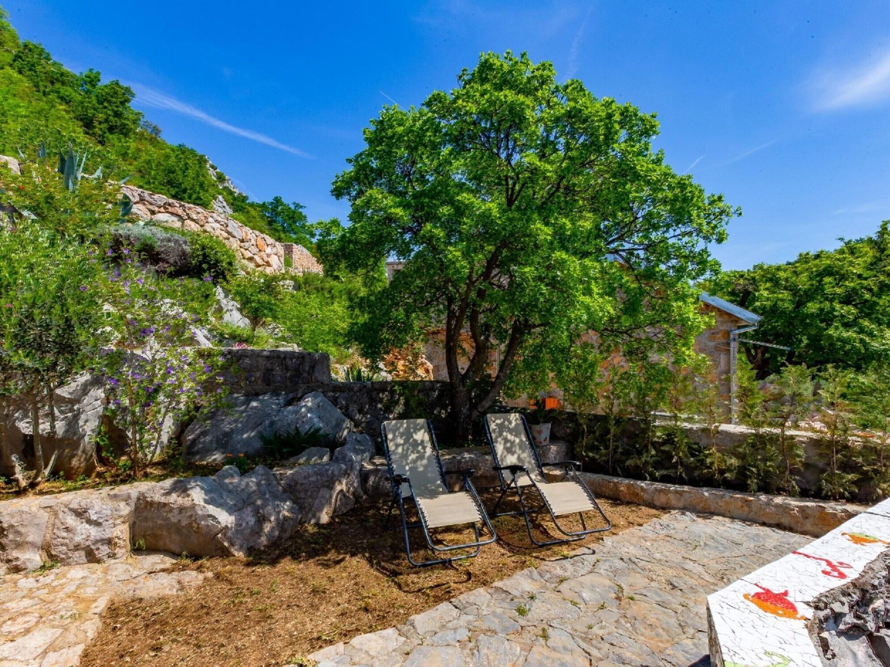 A stone patio with two lounge chairs, a tree, and a stone wall.