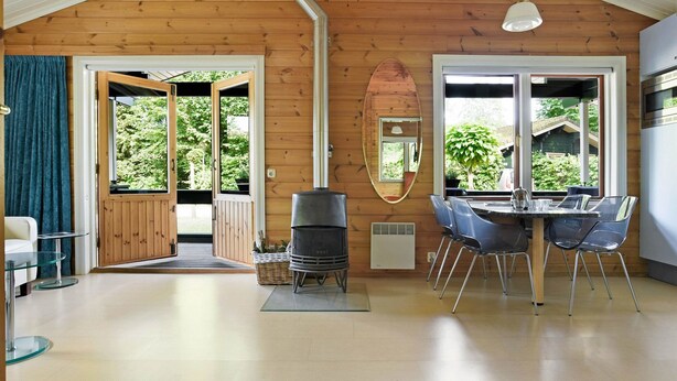 A spacious room with a wooden ceiling, a large dining table with chairs, a built-in oven, and a sliding glass door leading to an outdoor area. - Finnish Chalet with Private Garden & Sauna near Veluwe (Hulshorst)