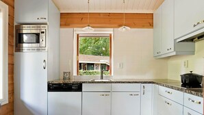 A modern kitchen with white cabinets, a built-in microwave, and a window overlooking a house. - Finnish Chalet with Private Garden & Sauna near Veluwe (Hulshorst)