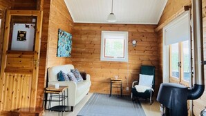 A cozy cabin interior with a wooden interior, a white ceiling, a sofa, a chair, a small table, and a window. - Finnish Chalet with Private Garden & Sauna near Veluwe (Hulshorst)