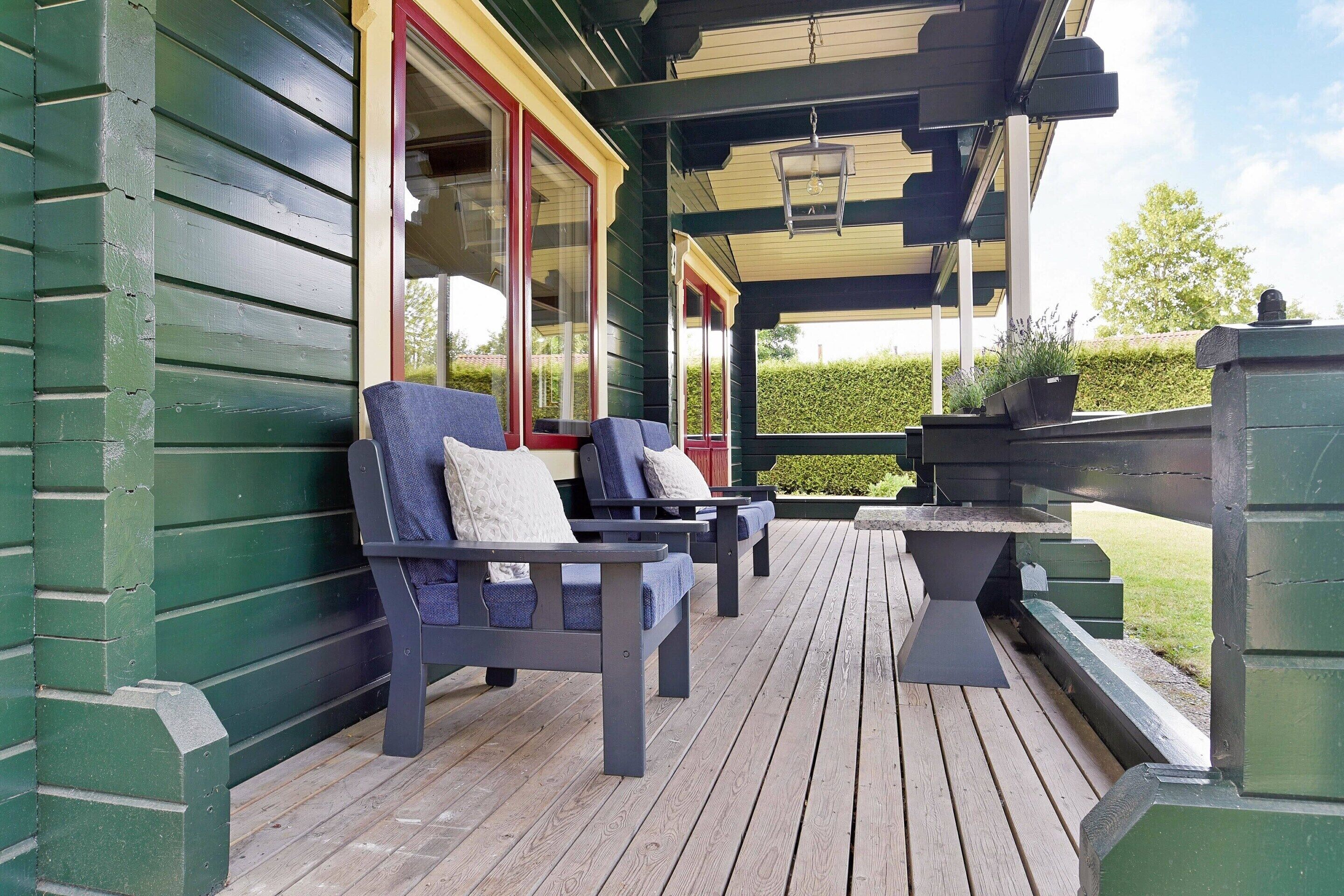 Een overdekt terras met houten vloer, twee donkerblauwe stoelen met kussens en een stenen tafel.