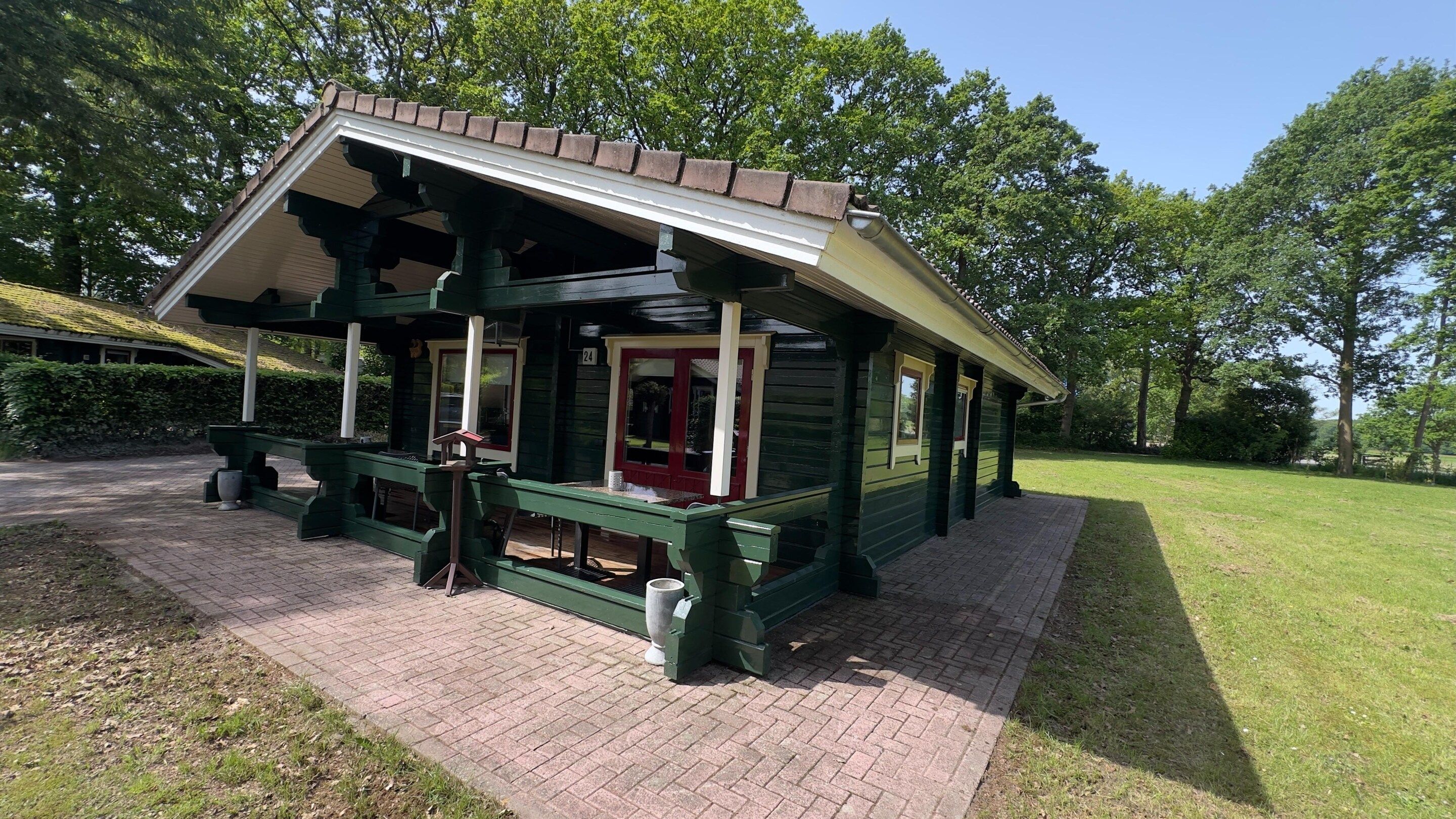 A wooden building with a sloped roof, a porch with benches, and a paved entrance area.