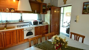 A kitchen with wooden cabinets, a stove, a microwave, and a dining table with chairs. - Belvilla by OYO Casa Rosada (Pompei)