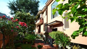 A courtyard with potted plants, a pathway, and a building with a balcony. - Belvilla by OYO Casa Rosada (Pompei)
