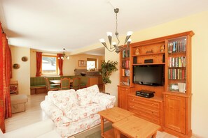 A cozy living room with a sofa, wooden cabinet, and television. There's a dining area with a table and chairs in the background. - Chalet in Saalbach for 10 Guests (Saalbach-Hinterglemm)