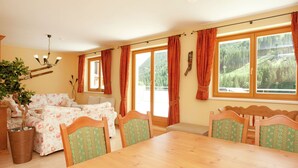 Una sala acogedora con una mesa de comedor de madera, sofá floral y ventanas amplias con cortinas.