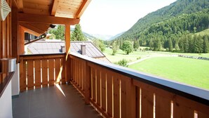 Un balcón de madera con vistas a un valle verde y montañas boscosas.