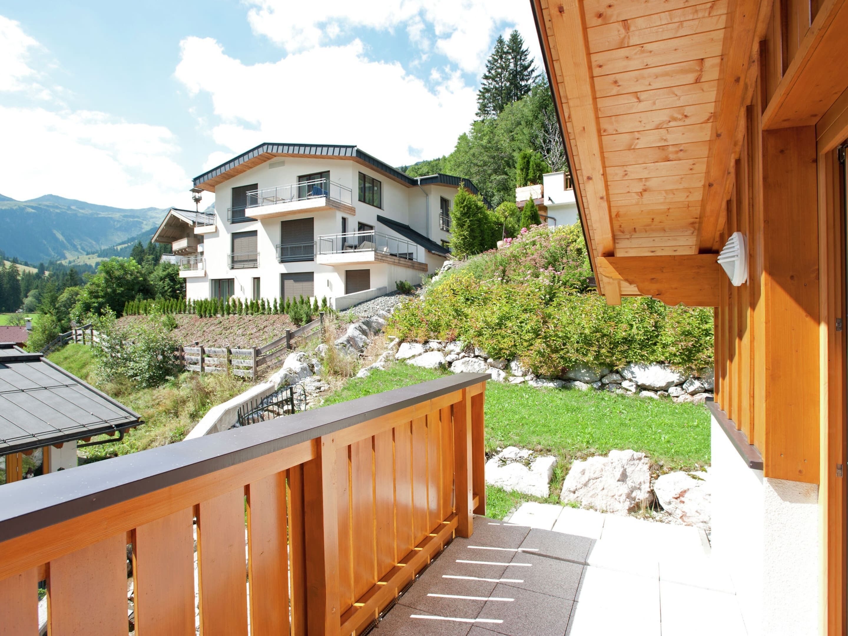 Ein Holzbalkon mit Blick auf ein modernes, mehrgeschossiges Gebäude und eine Berglandschaft.