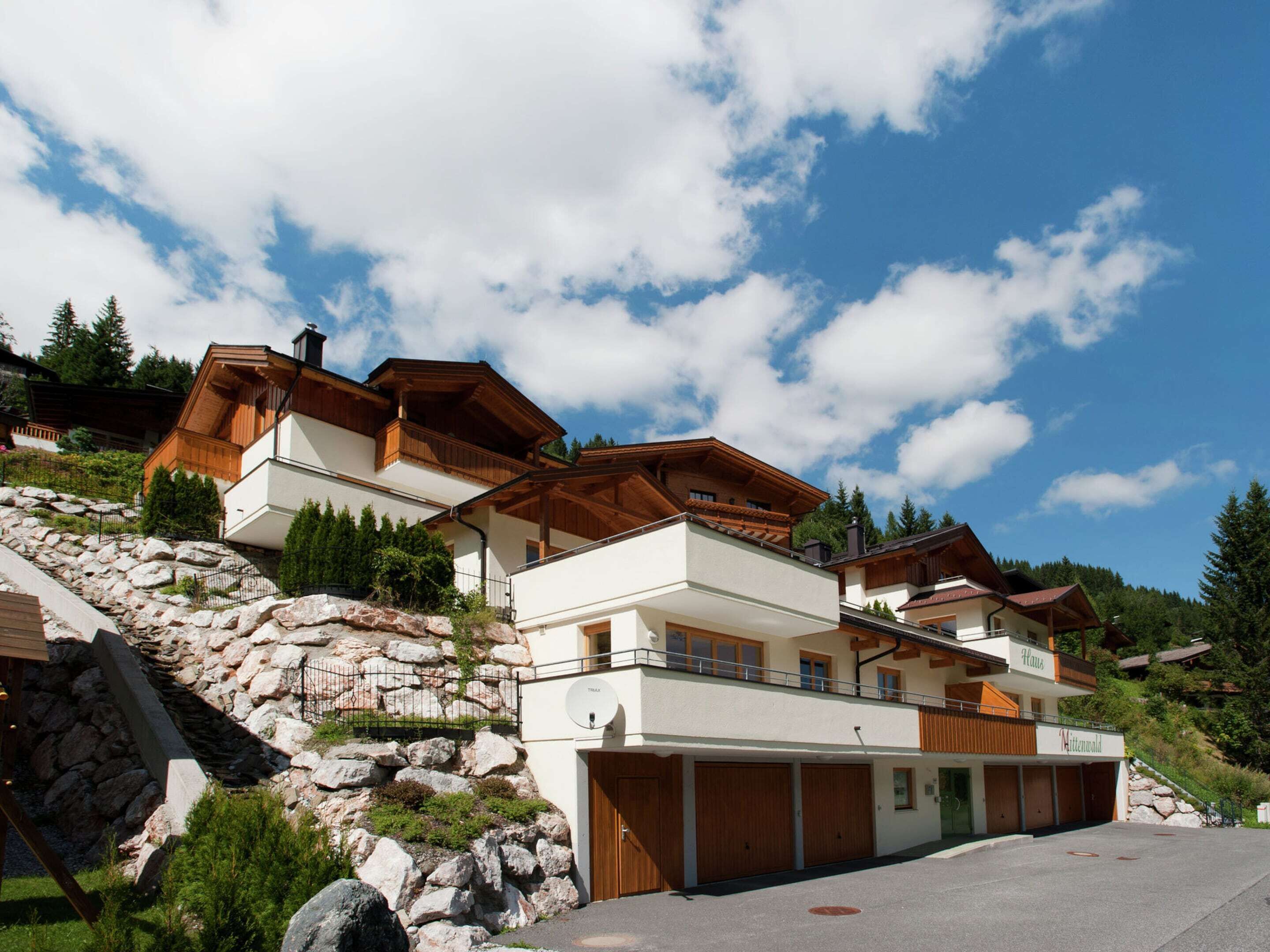 A modern chalet with a stone retaining wall, wooden balconies, and a garage.