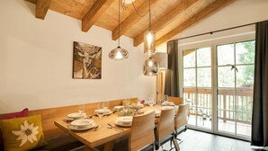 A dining area with a wooden table set for six, a painting on the wall, and a large window with a view of greenery. - Luxurious Holiday Home With Sauna (Krimml)