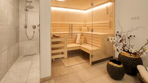 A modern sauna room with wooden benches, a glass door, and a shower area. - Luxurious Holiday Home With Sauna (Krimml)