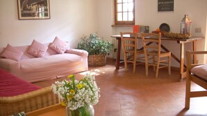 Una sala de estar acogedora con un sofá, una mesa de comedor con sillas, un jarrón de flores y una estantería.