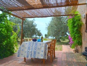 An outdoor patio with a table set for two, surrounded by olive trees and a pergola. - Holiday Home Monte Argentario Sea Views (Monte Argentario)