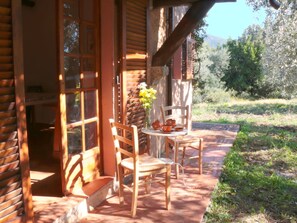 Une cabane en bois avec une véranda, deux chaises en bois, une petite table et un vase rempli de fleurs.