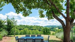 An outdoor dining area with a table and chairs under a tree, surrounded by a grassy landscape and trees. - Tranquil Holiday Home With Private Pool (Teillots)