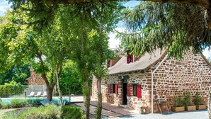 A stone building with a red door, surrounded by greenery and a pool. - Tranquil Holiday Home With Private Pool (Teillots)