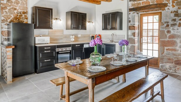 A rustic kitchen with stone walls, wooden beams, and a wooden table set for dining. - Tranquil Holiday Home With Private Pool (Teillots)