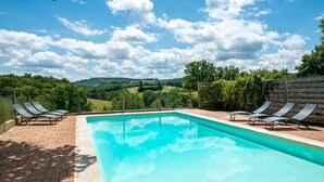 A rectangular swimming pool with clear blue water, surrounded by a brick patio. There are four lounge chairs on the patio, and a wooden fence with climbing plants in the background. - Tranquil Holiday Home With Private Pool (Teillots)