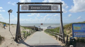 A beach entrance sign labeled "Entree Strand" with a pathway leading to the beach.