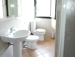 A bathroom with a white sink, toilet, and a window with a view. - Residence with Swimming Pool in Green Countryside near Thermal Baths (Santa Maria Coghinas)