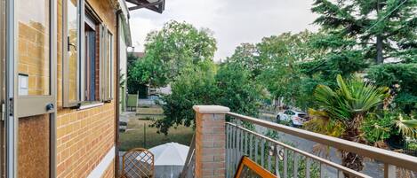 A balcony with a wooden bench, a potted plant, and a view of a street with cars and trees.