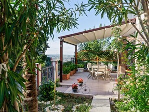 A covered patio with outdoor furniture, a view of the countryside, and a garden area with plants and a small water feature. - Spacious Apartment near Saludecio (Saludecio)