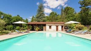 A swimming pool with lounge chairs and umbrellas, surrounded by trees and a building with a tiled roof. - Holiday Home in Bourgnac With Private Pool (Bourgnac)