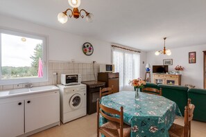 A compact kitchen with a washing machine, microwave, and a dining area with a table and chairs. - Priziac Garden Hideaway (Priziac)