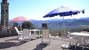 A terrace with outdoor seating, a clock tower, and a scenic mountain view. - Apartment in Rio Near Roman Bridge (Sesta Godano)