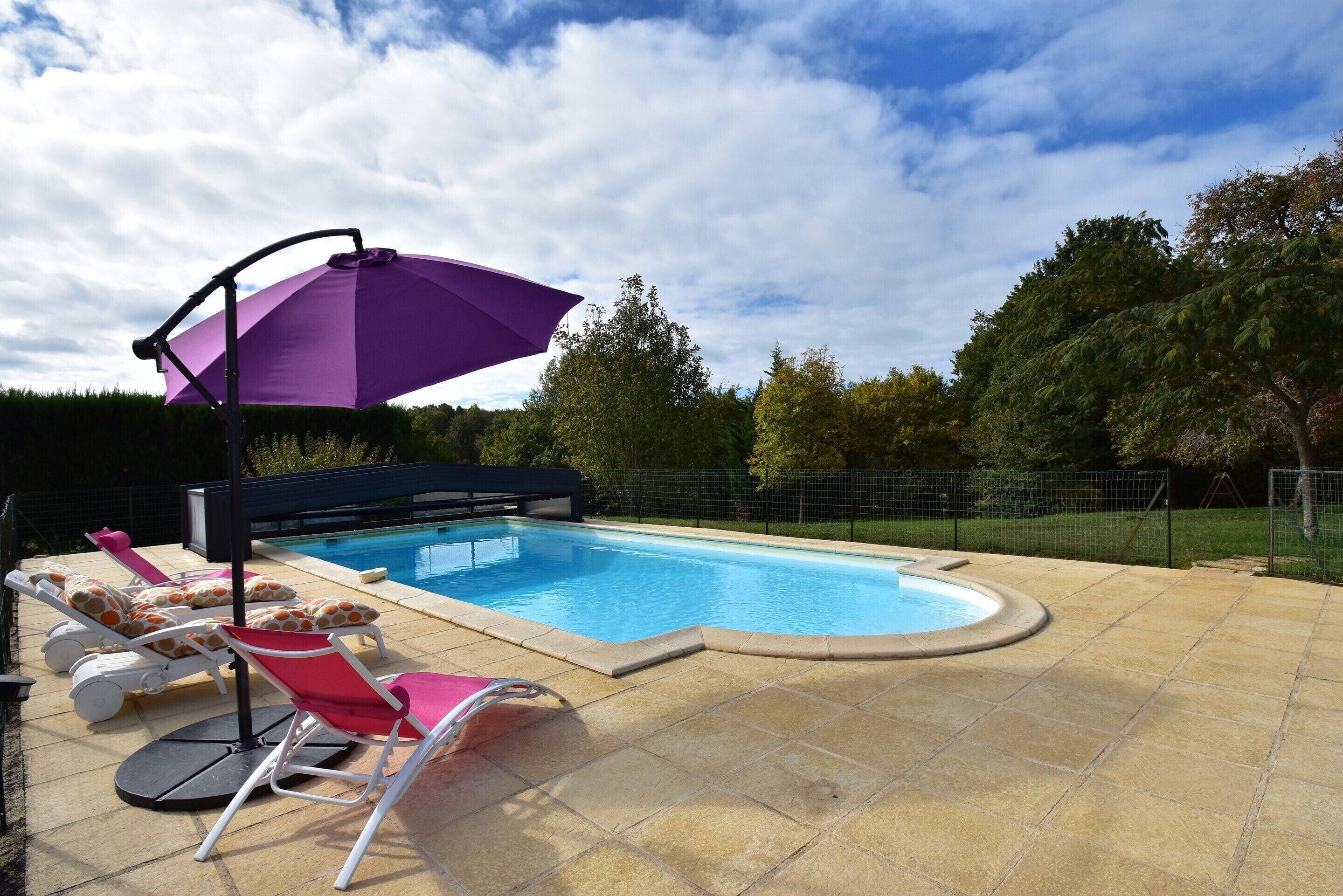 A swimming pool with lounge chairs and a purple umbrella.