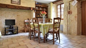 A dining area with a table set for four, surrounded by wooden chairs, a television on a stand, and a stone wall with a wooden beam. - Spacious Holiday Home With Private Pool (Uzech)