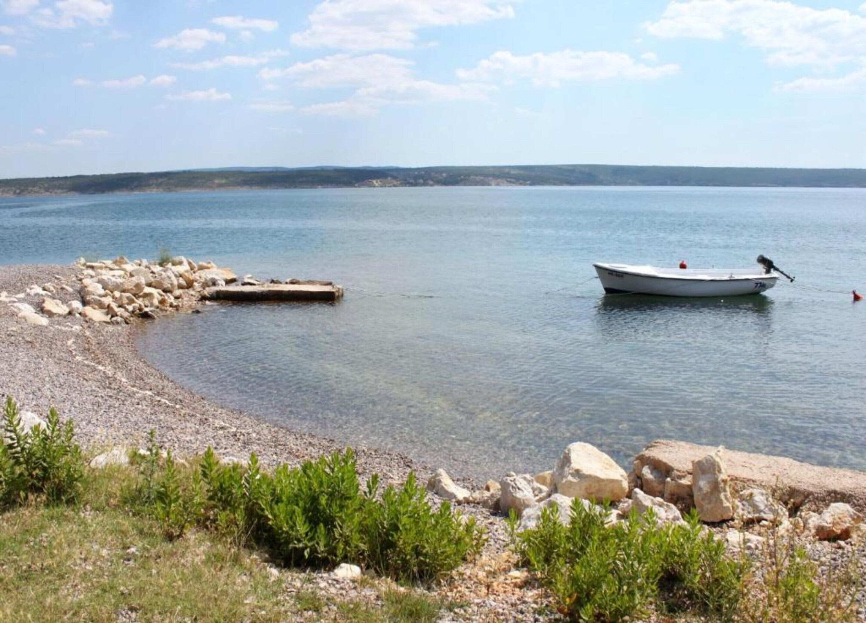 A boat on a calm lake with a rocky shoreline and sparse vegetation.