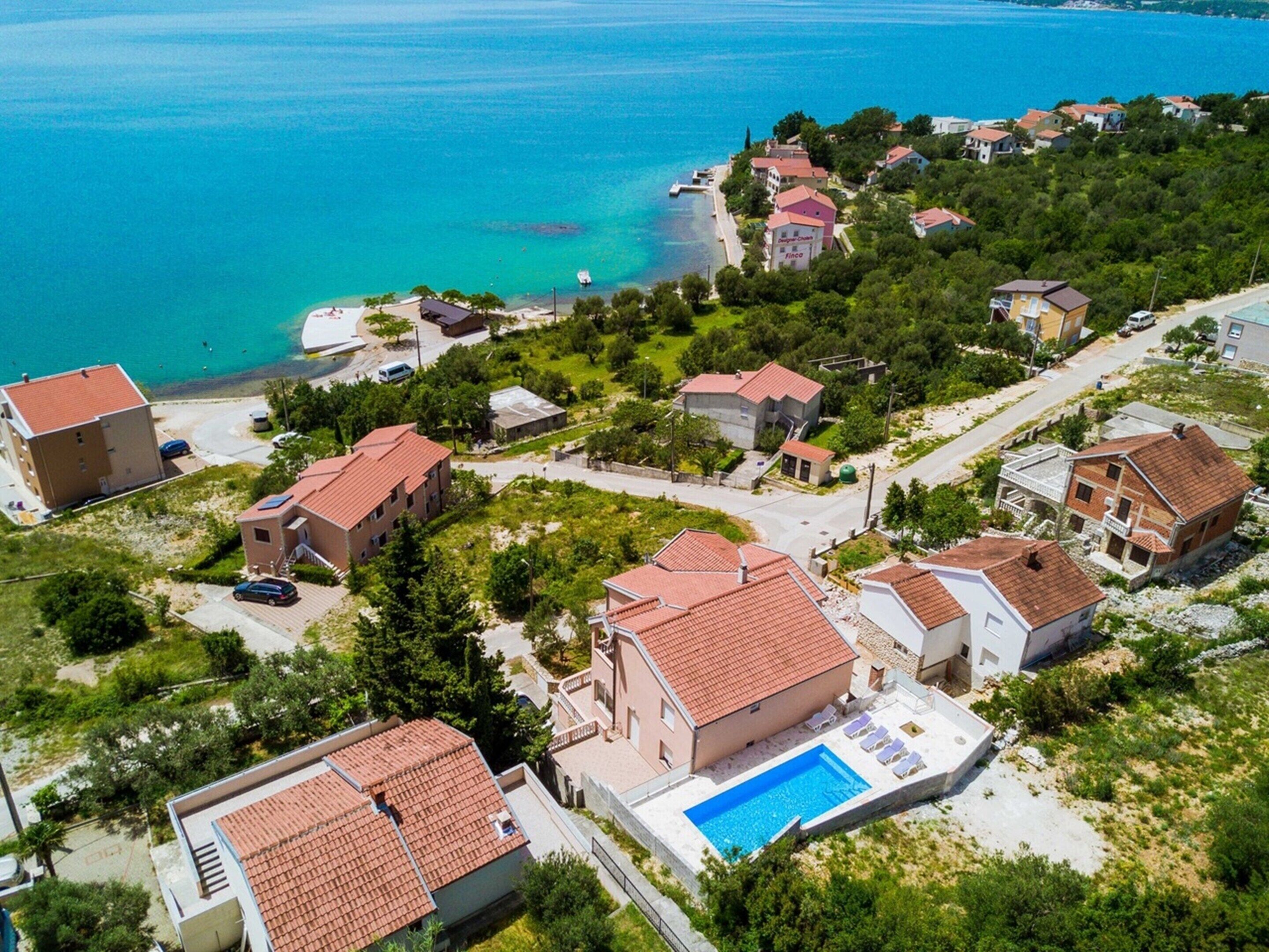 An aerial view of a coastal residential area with houses, a swimming pool, and a beach.