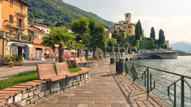 A riverside walkway with benches, a stone wall, and a bridge. - Belvilla by OYO Romantica (Gravedona)