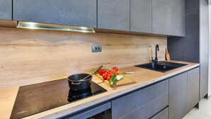A modern kitchen with a wooden countertop, a black induction cooktop, a sink, and grey cabinets. - Holiday Home Bibinje Near the Sea (Bibinje)