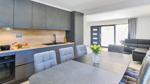 A modern kitchen with grey cabinets, a wooden countertop, and a built-in oven. There is a dining area with a grey table and chairs, and a black sofa. - Holiday Home Bibinje Near the Sea (Bibinje)