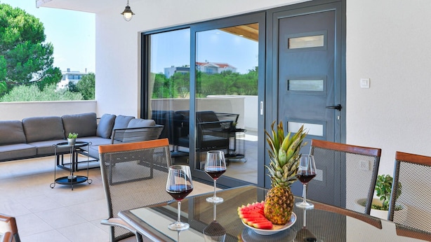 An outdoor seating area with a table set for two, featuring a pineapple and watermelon, and two glasses of red wine. - Holiday Home Bibinje Near the Sea (Bibinje)