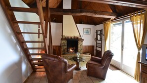 A cozy room with a fireplace, wooden beams, a staircase, and leather chairs. - Normandy Bakery Retreat (Torigny-les-Villes)