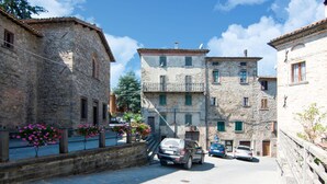 Una calle estrecha con edificios de piedra, coches aparcados y macetas con flores.