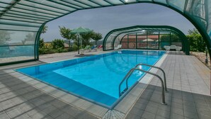 Una piscina interior con techo de vidrio, rodeada de suelo de baldosas y algunas sillas de descanso.