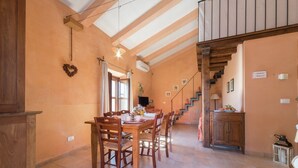 Ein geräumiger Essbereich mit hoher Decke und freiliegenden Balken, eine Treppe, die zu einer oberen Ebene führt, sowie eine Küchenzeile mit Holzausziehtisch und Schränken.