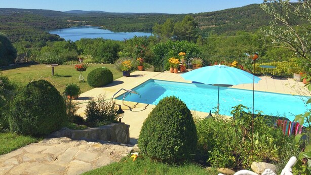 A swimming pool with a blue umbrella, surrounded by greenery and a view of a lake. - Verdon Views: Pool & Terrace (Montagnac-Montpezat)
